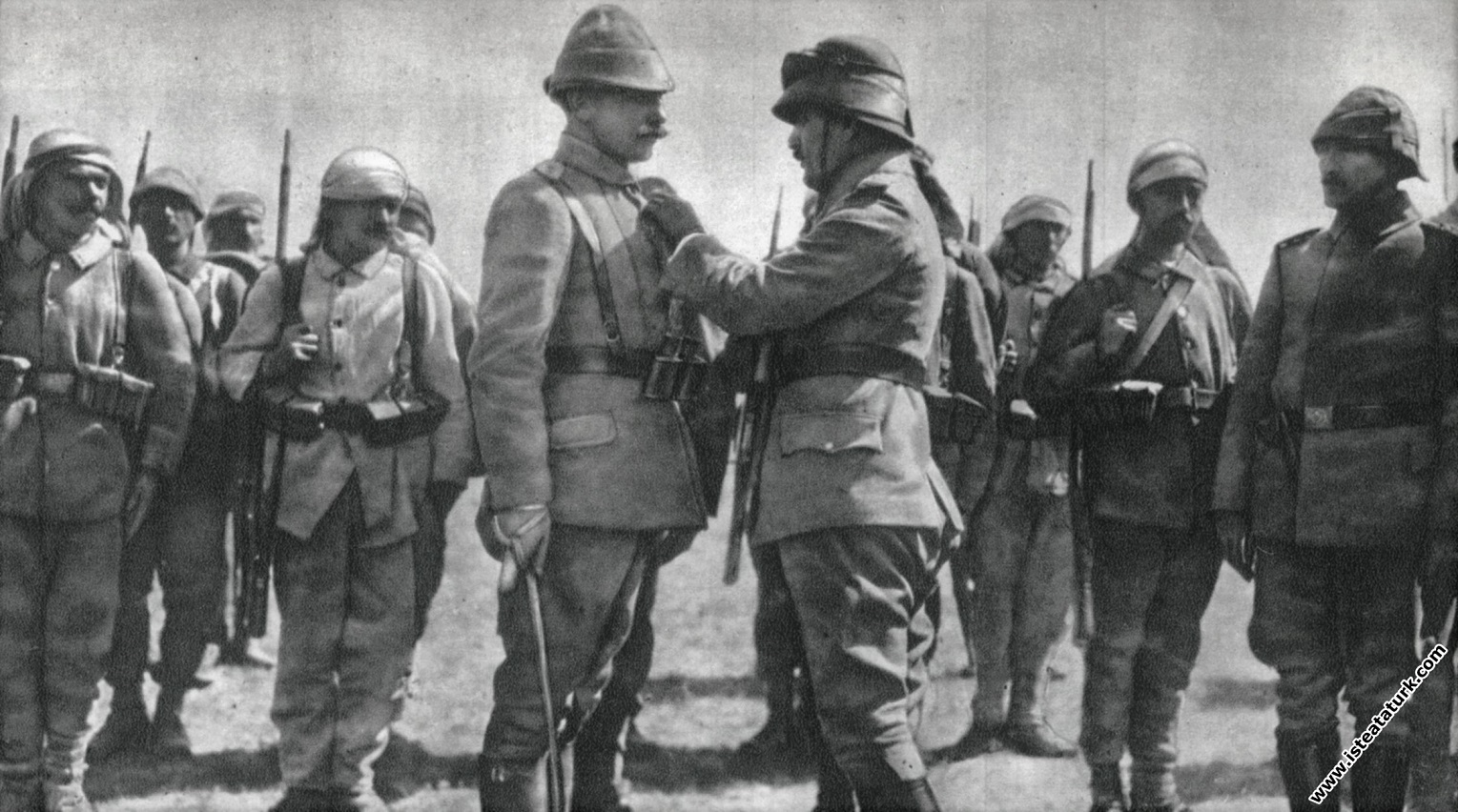 Mustafa Kemal, Harbiye Nazırı Enver Paşa'nın emrindeki subaylardan birine madalyasını takarken, tören alanında. (1915)